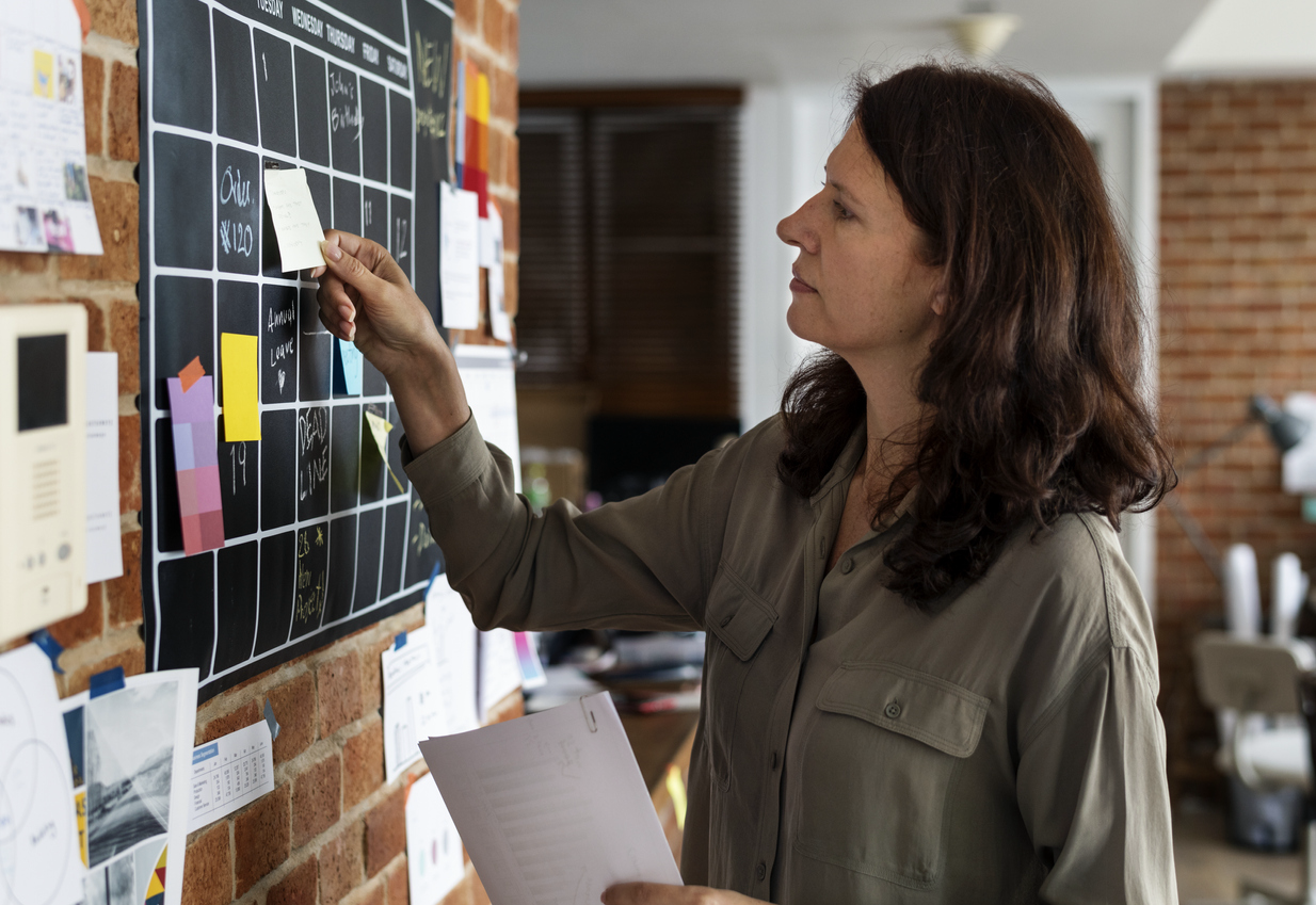 woman looking at her monthly wall calendar and putting up reminder notes