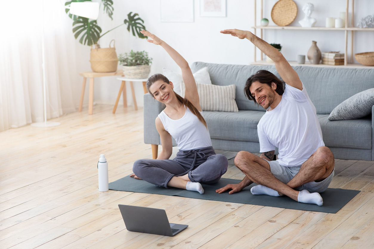 woman and man doing yoga on a mat in front of laptop