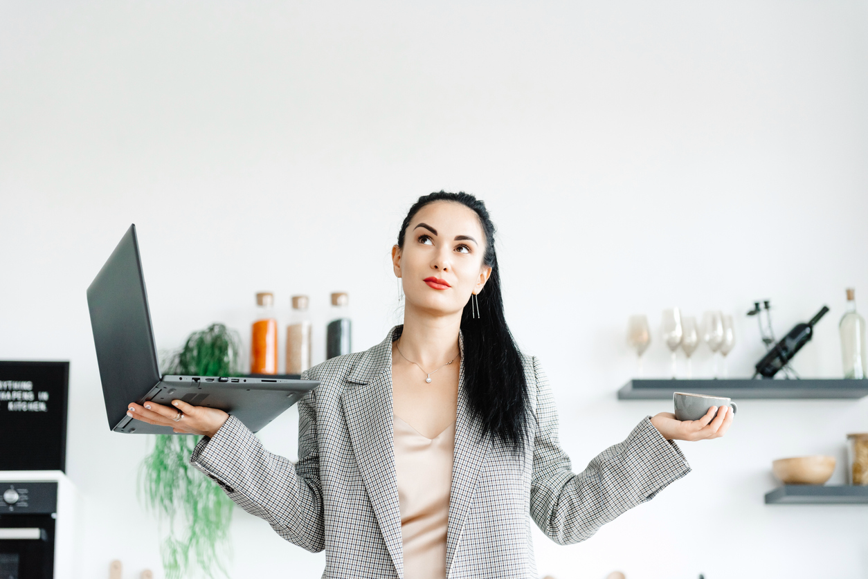 woman looking up and thinking while holding her laptop in one hand and coffee in other hand