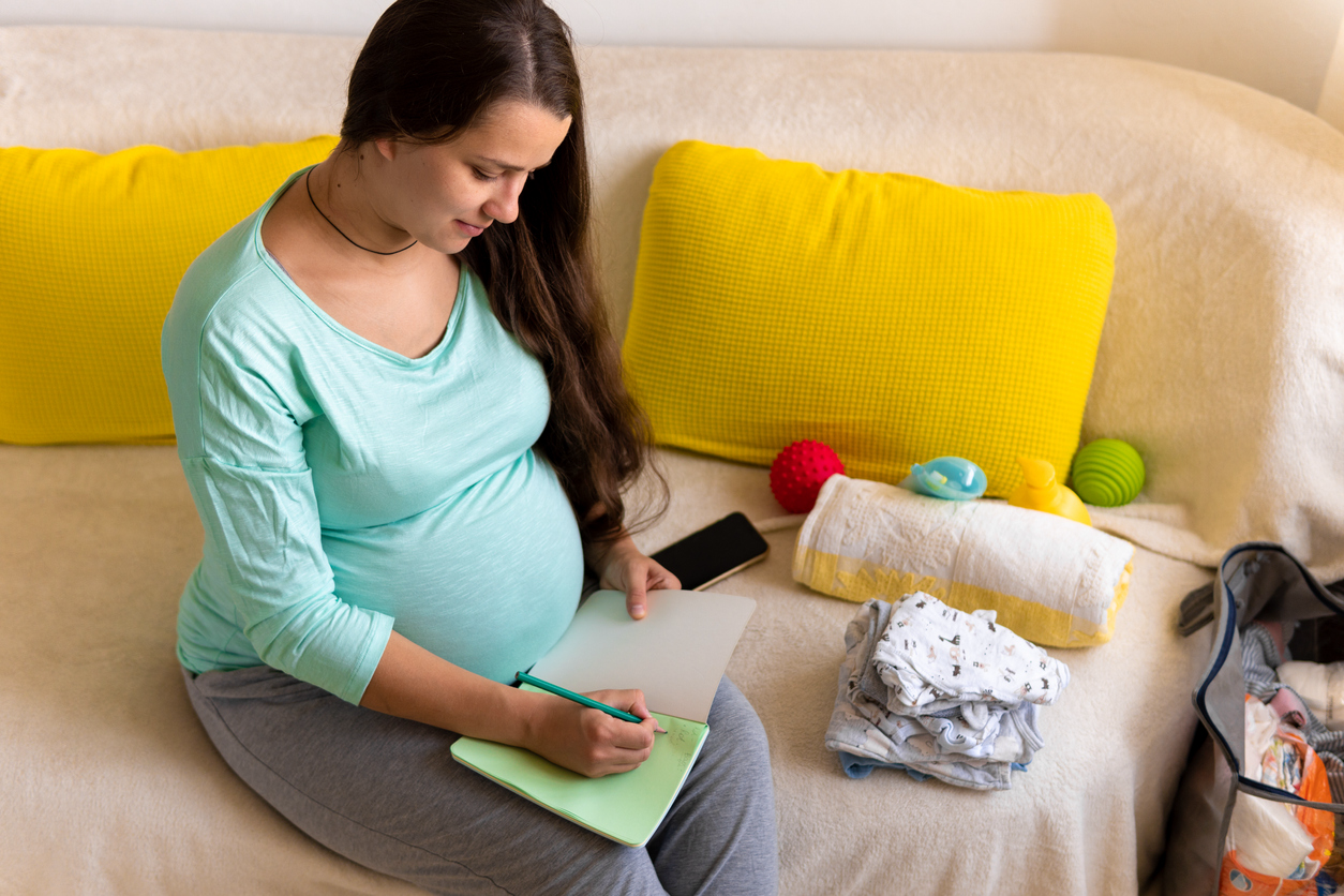 pregnant women sitting on couch with baby products and writing in notebook 